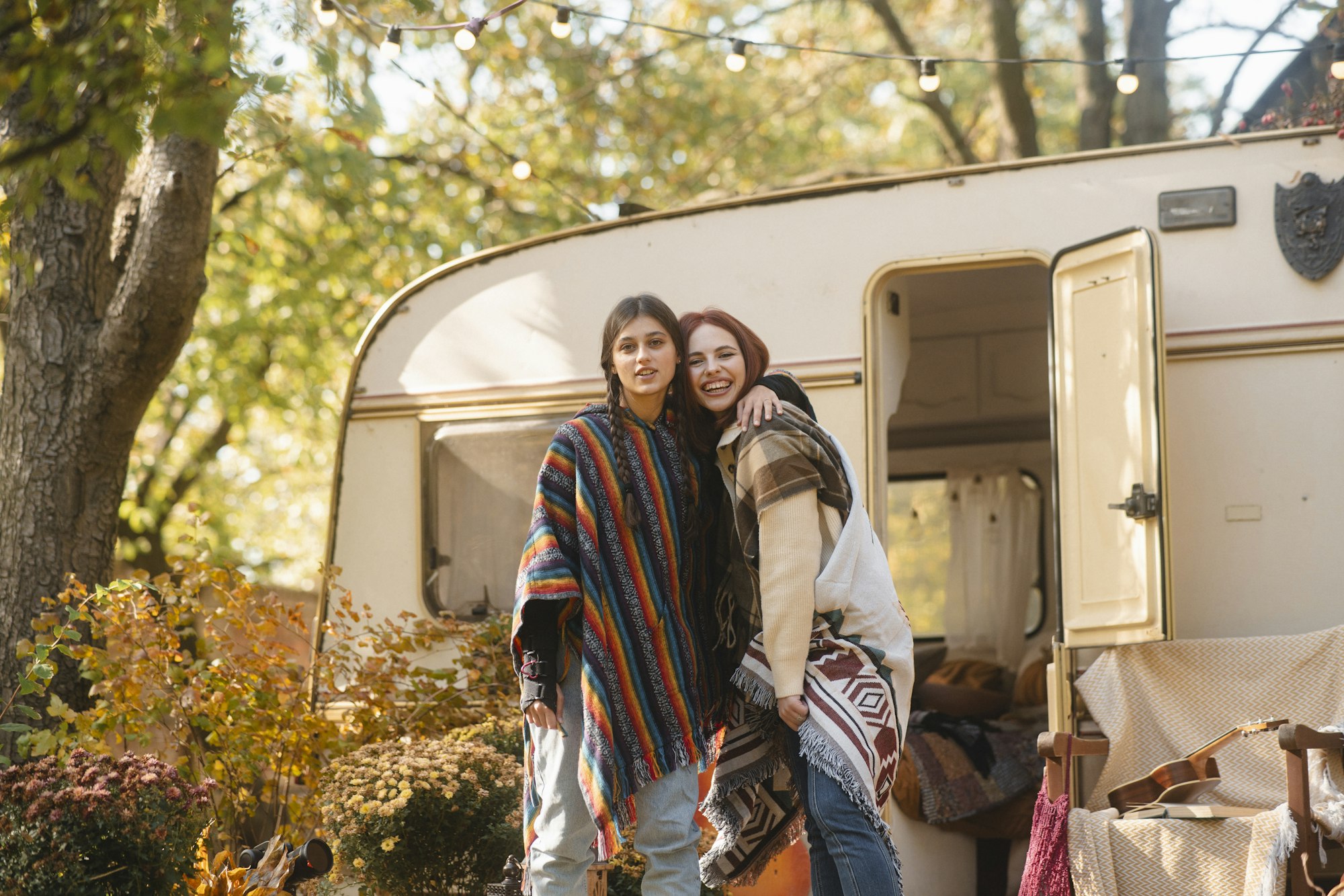 Two stylish girls in hippie attire pose against the backdrop of a trailer.